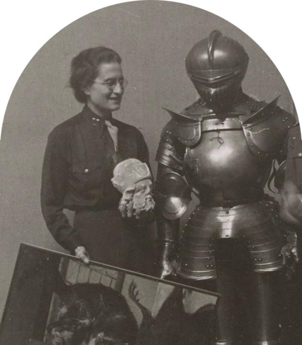 An arch-shaped black-and-white photograph of a woman in a button-down uniform standing next to a suit of armor and holding a sculpture fragment of a human head in her left hand and a painting in her right hand.